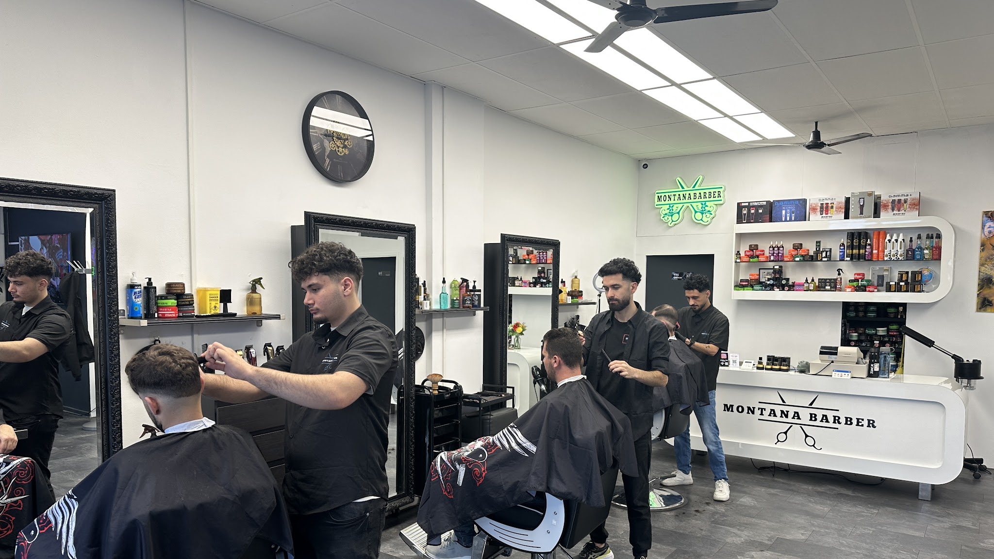 Drie barbiers aan het werk bij Montana Barber, met het groene neonbord en de belettering op de toonbank