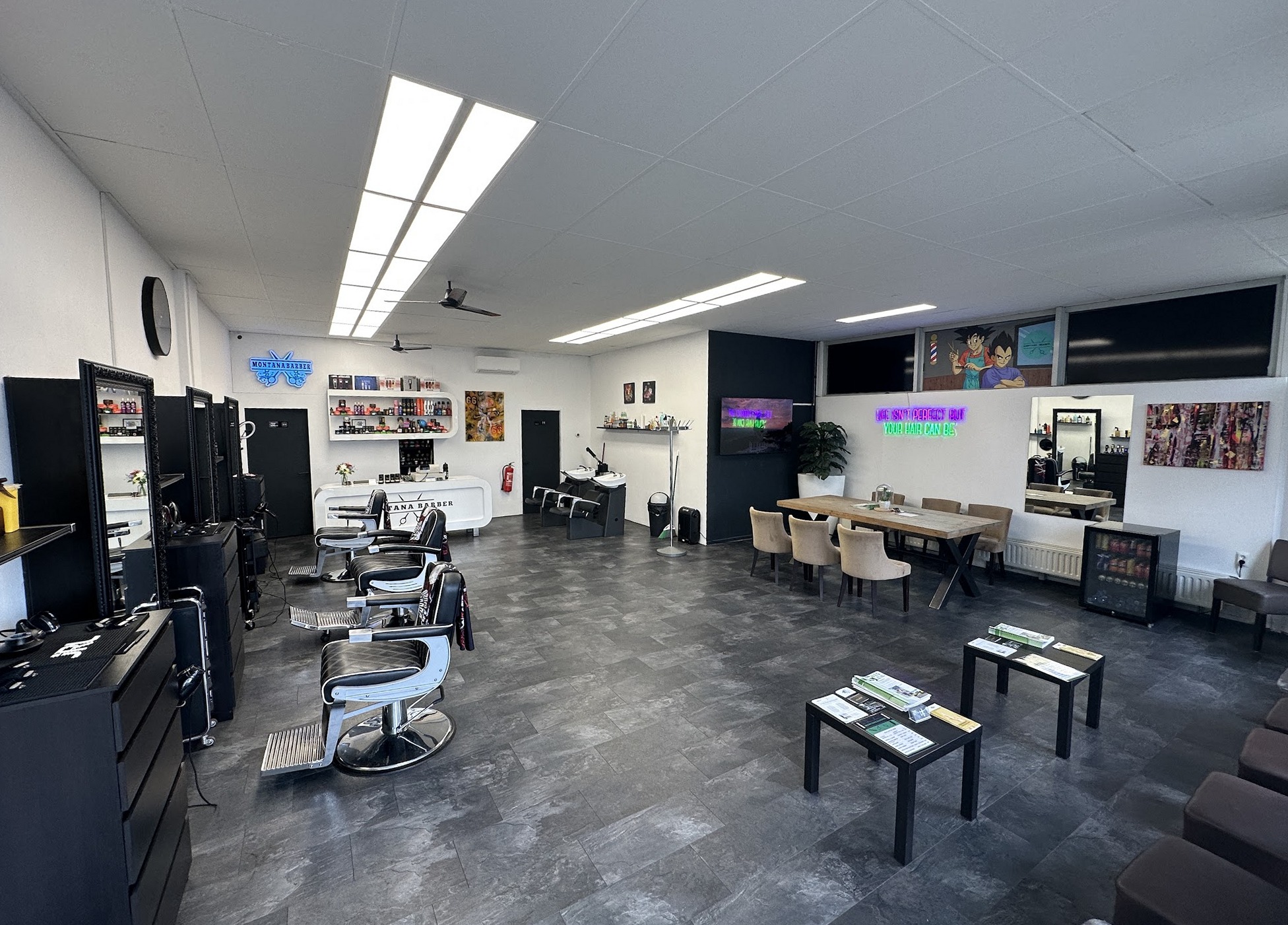 Het interieur van Montana Barber: drie barbierstoelen voor spiegels, de wachthoek met tafel en neon aan de muur