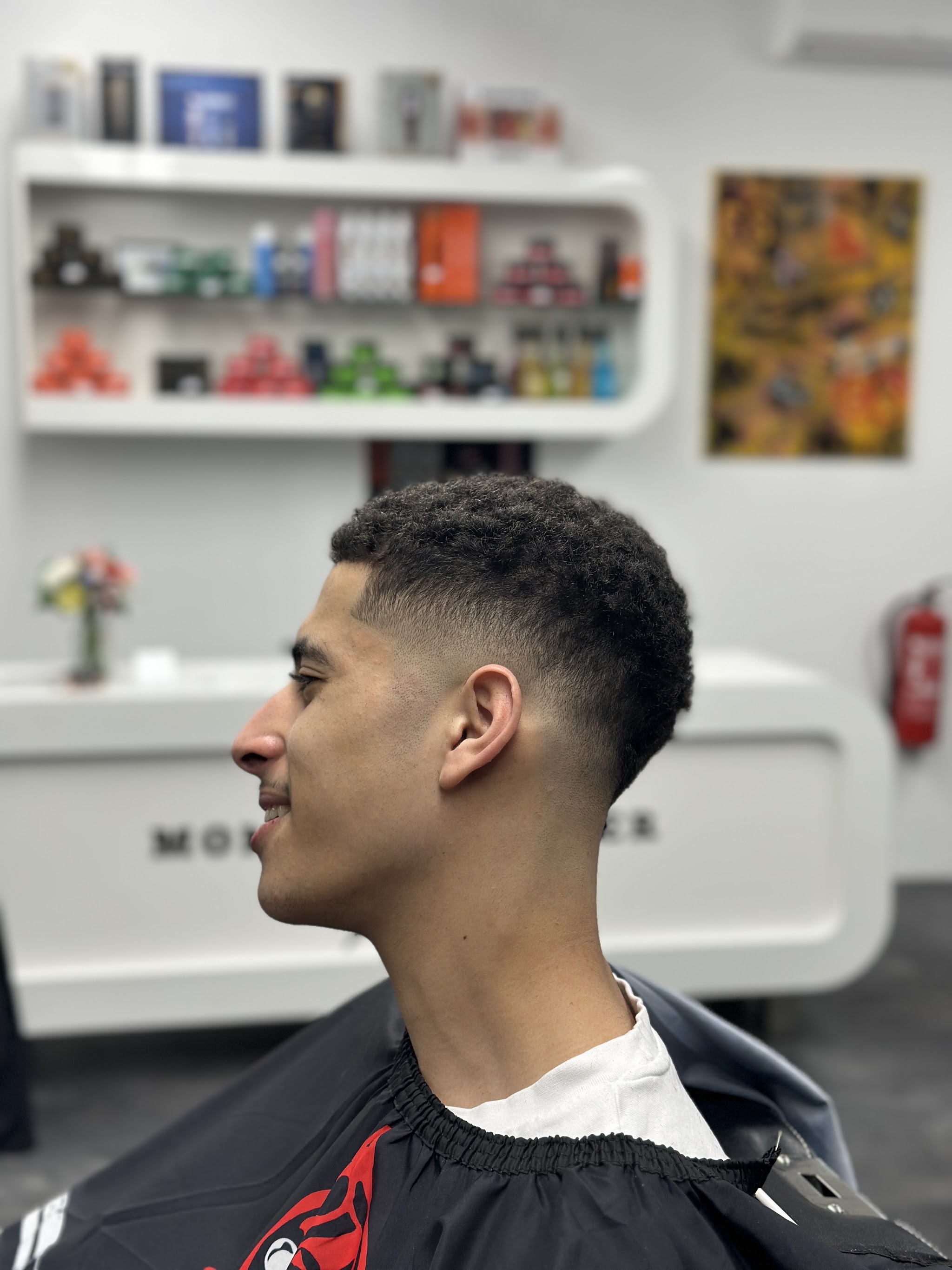 Skin fade met korte krullen, de toonbank met belettering op de achtergrond